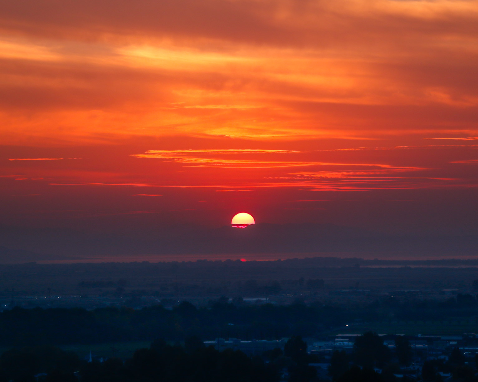 the sun begins to set lighting the sky red and somehow throwing the town and trees in blue shadow